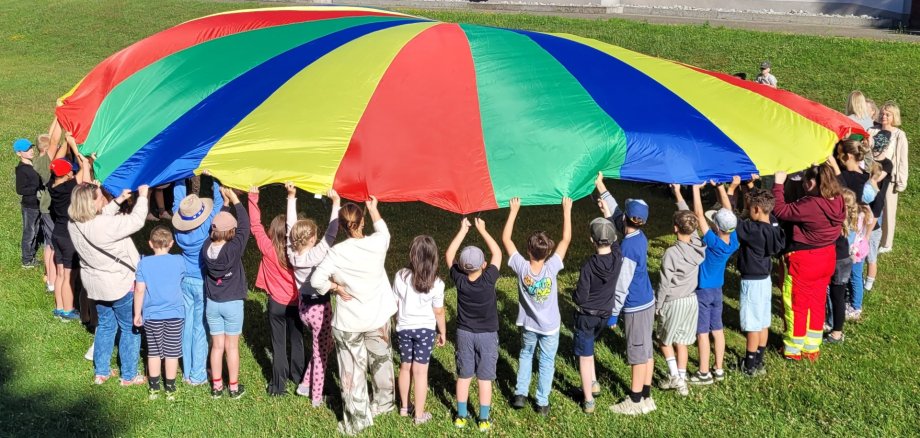 Kunterbunt, wie das Riesenschwungtuch waren auch die Angebote für die Kinder aus der Verbandgemeinde, auf dem bestens geeigneten Nisterauer Gelände, wo alle gemeinsam ganz viel Spaß miteinander hatten. Teilnehmer halten ein große buntes Tuch in die Luft.