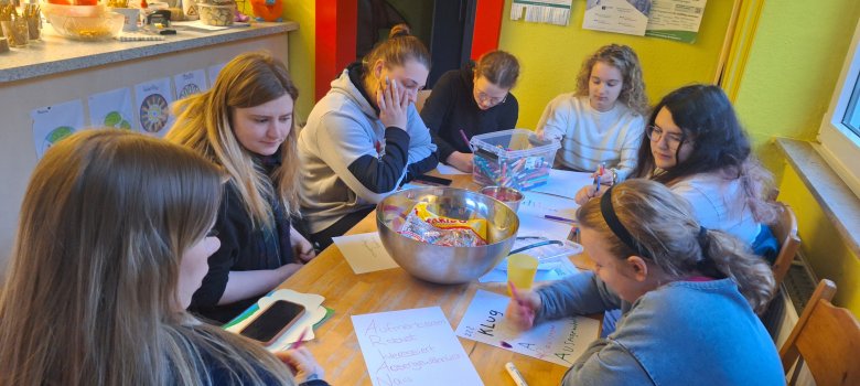 Um sich kennen zu lernen sammelten die Mädchen, als eine Übung, Adjektive zu den einzelnen Buchstaben ihrer Vornamen, die ihrer Meinung nach ihre Person beschreiben. Mädchen sitzen gemeinsam bei der Übung am Tisch.