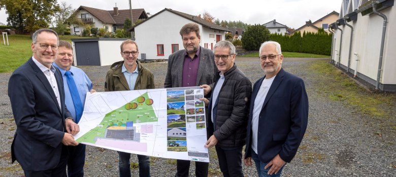 Ortsbürgermeister Thomas Ax und der Beigeordnete der Ortsgemeinde, Matthias Verhoeven, stellen Ebling und Hering die Maßnahme auf dem „Kirmesplatz“ vor.