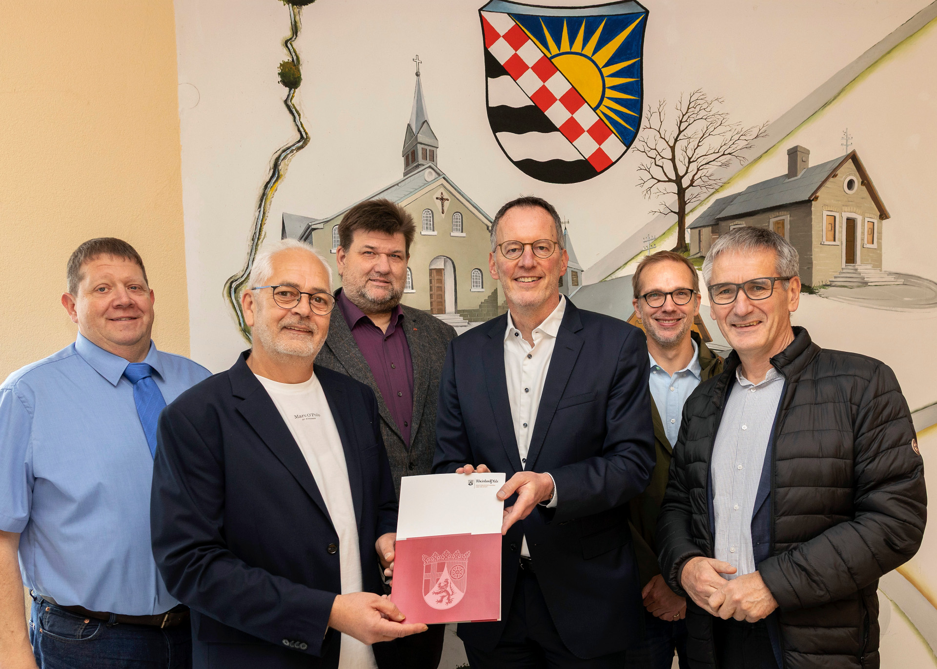 Innenminister Ebling überreicht Ortsbürgermeister Thomas Ax die Bewilligungsbescheide. Mit dabei von rechts: Landtagsabgeordneter Hendrik Hering (SPD), Architekt Philipp Alhäuser, der VG-Beigeordnete Thomas Mockenhaupt und der Beigeordnete der Ortsgemeinde Matthias Verhoeven.